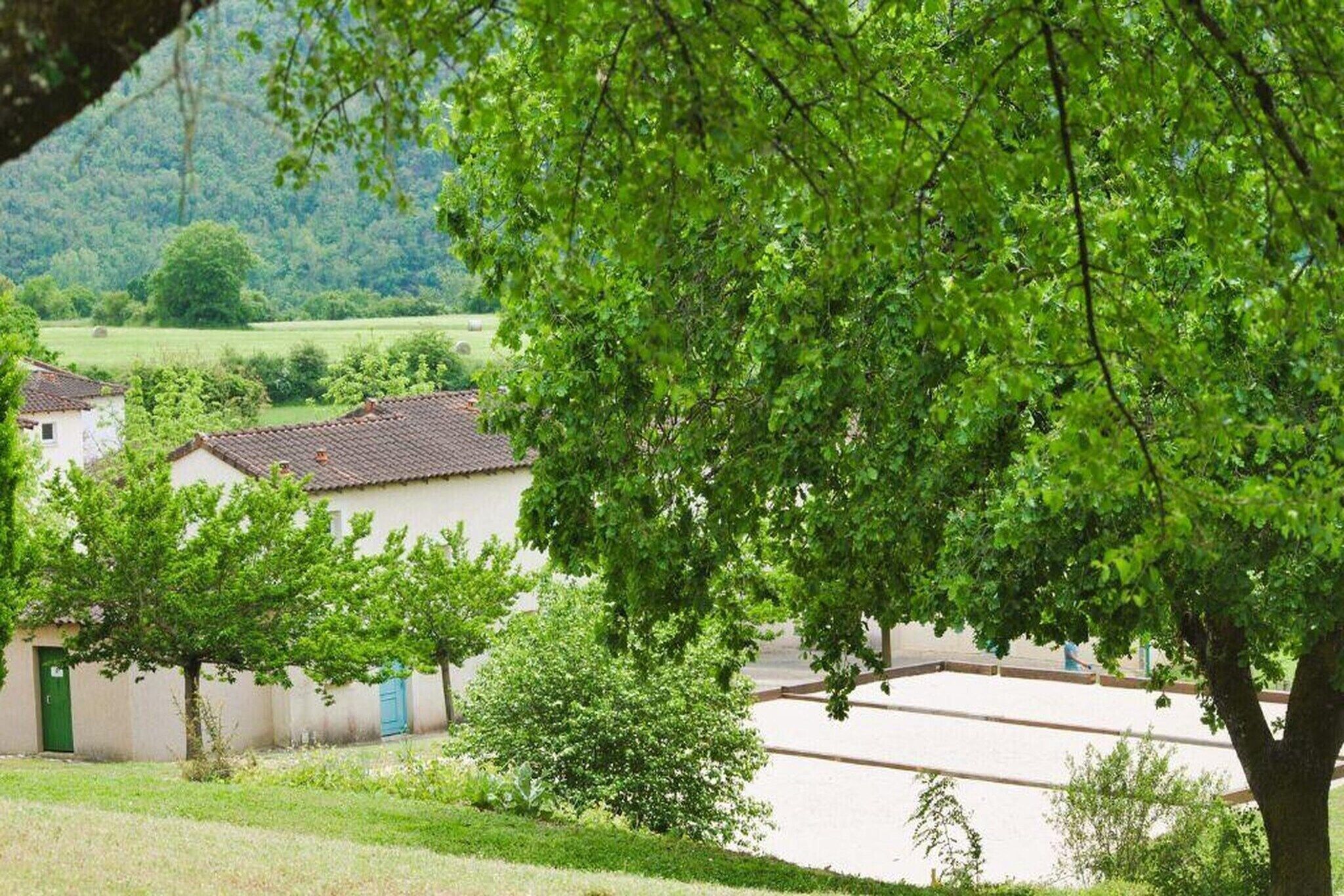 A rural village with traditional buildings, a tree-lined street, and a view of the countryside.