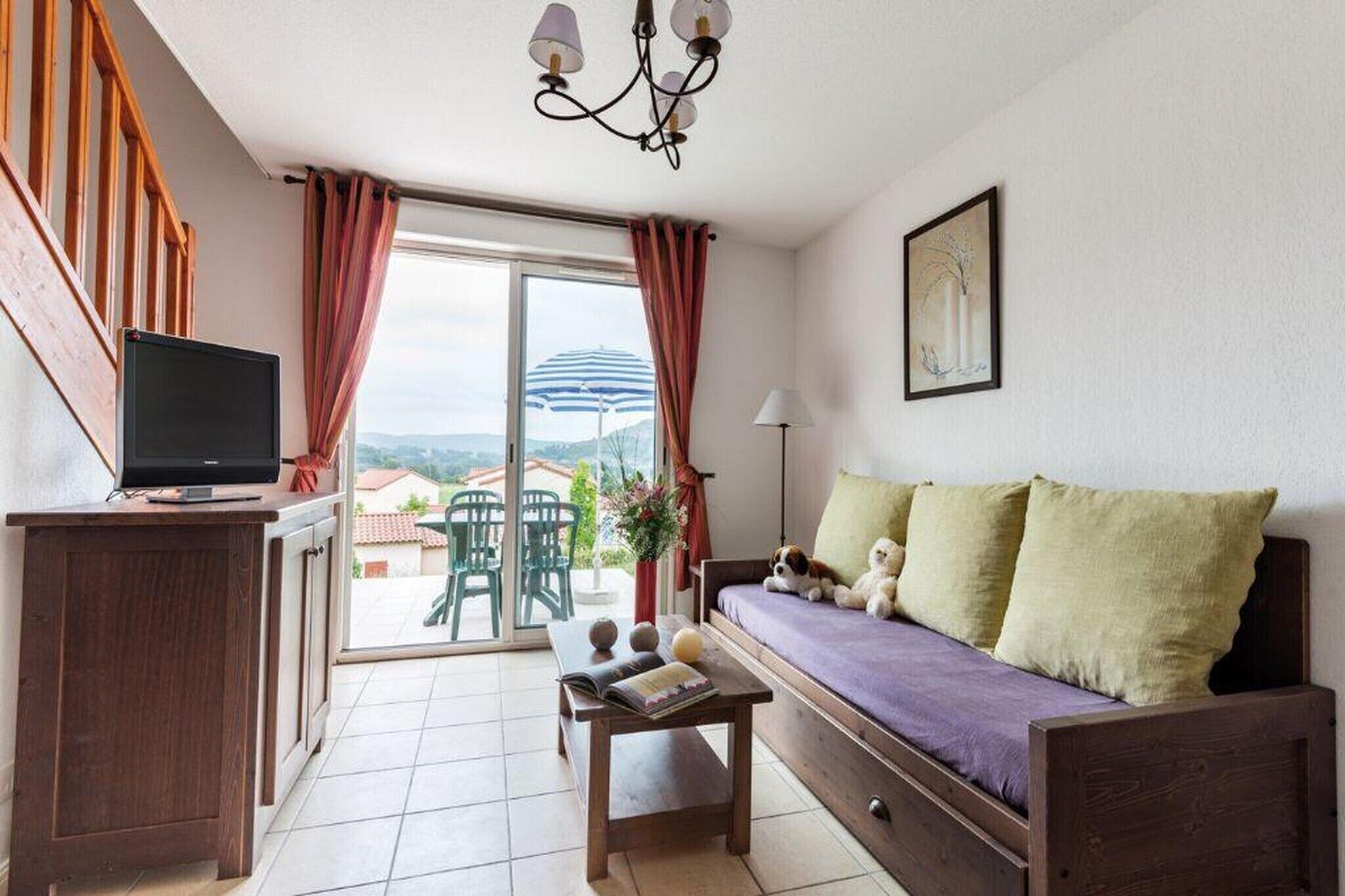 Un espacio de estar con sofá, televisor, una mesa con libros y vistas al exterior.