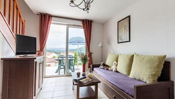 Un espacio de estar con sofá, televisor, una mesa con libros y vistas al exterior.