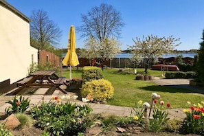 Ein Garten mit einem Holztisch und Stühlen, einem gelben Sonnenschirm und verschiedenen Blumen.