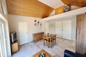 Un vaste espace de vie doté d’un plafond en bois, d’une table à manger avec des chaises, d’un téléviseur posé sur un meuble et d’une grande armoire en bois.