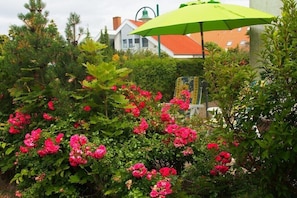 A garden with pink flowers and a green umbrella. - Holiday home in Rerik with swimming pool (Rerik)