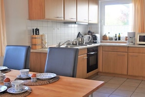 A kitchen with wooden cabinets, a sink, a stove, and a window with curtains. - Holiday home in Rerik with swimming pool (Rerik)