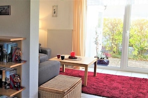 A living room with a sofa, a table with a red candle, a bookshelf, and a view through a glass door. - Holiday home in Rerik with swimming pool (Rerik)