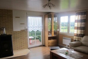 Ein Wohnzimmer mit Kamin, einer Couch, einem Tisch mit Lampe und Blick ins Freie.
