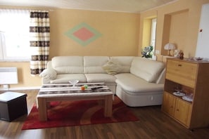 Ein Wohnzimmer mit Sofa, Couchtisch, Schrank und einem Fenster mit Vorhängen.