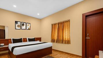 A hotel room with a large bed, a wooden headboard, a bedside table, a mirror, and a door.