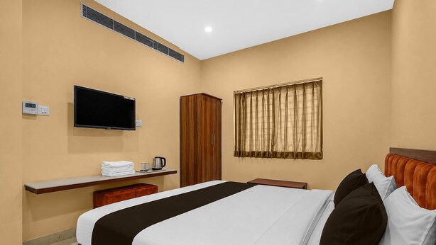 A hotel room with a bed, a TV, a desk with a kettle, and a window with curtains. - Classic JR Royals (Golmuri)
