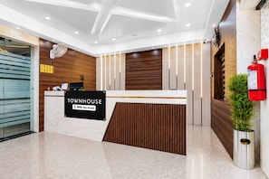 A reception desk with a sign reading 'TOWNHOUSE OYO-Serviced' in a modern lobby with wooden paneling and a marble floor. - Classic JR Royals (Golmuri)