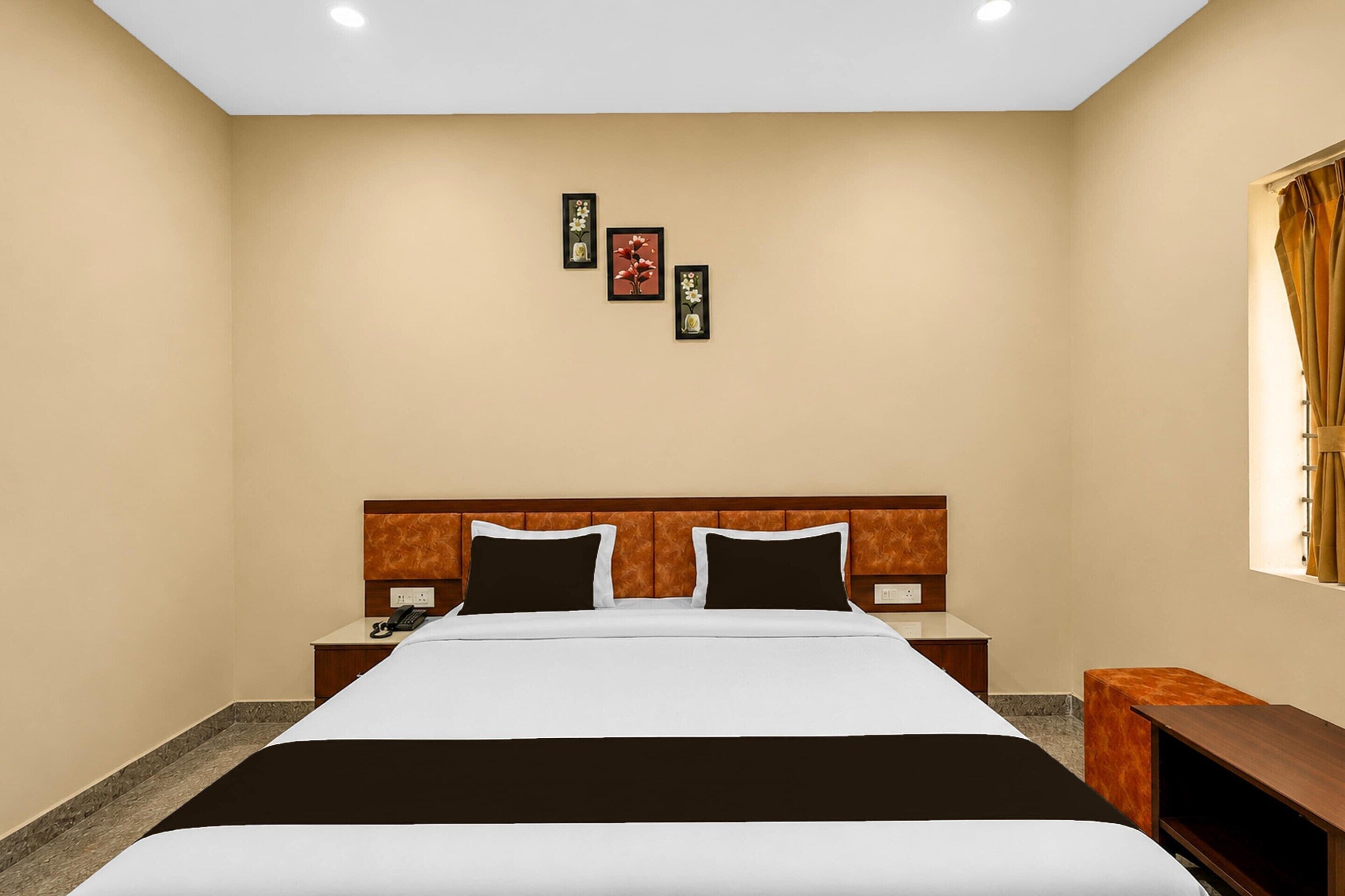 Une chambre d’hôtel comprenant un lit, des tables de chevet, une petite table, un téléphone fixé au mur et une fenêtre avec des rideaux.