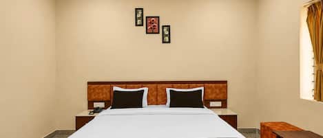 A hotel room with a bed, bedside tables, a nightstand, a wall-mounted telephone, and a window with curtains.