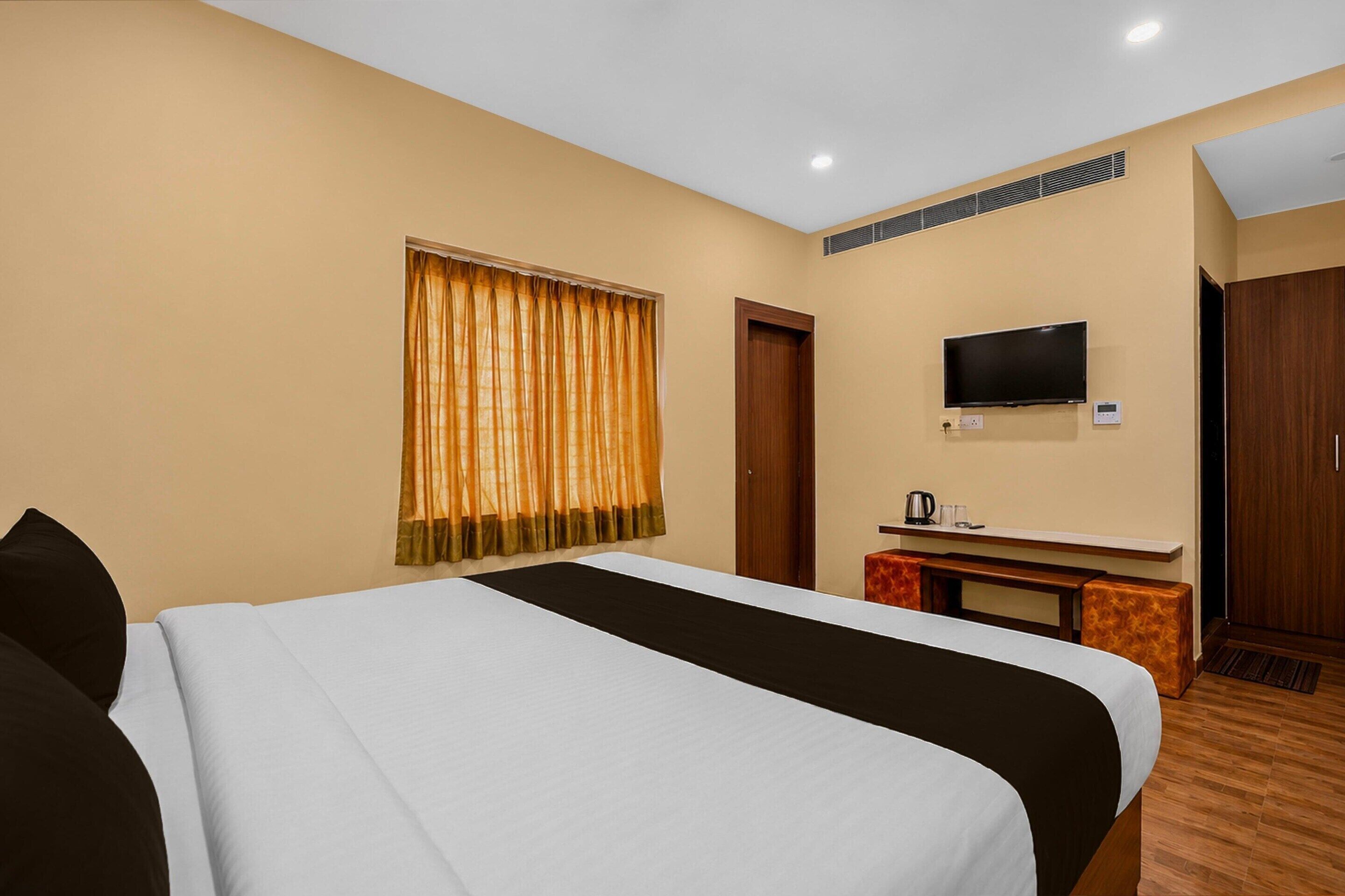 A hotel room with a bed, a television, a desk with a kettle, and a wardrobe.