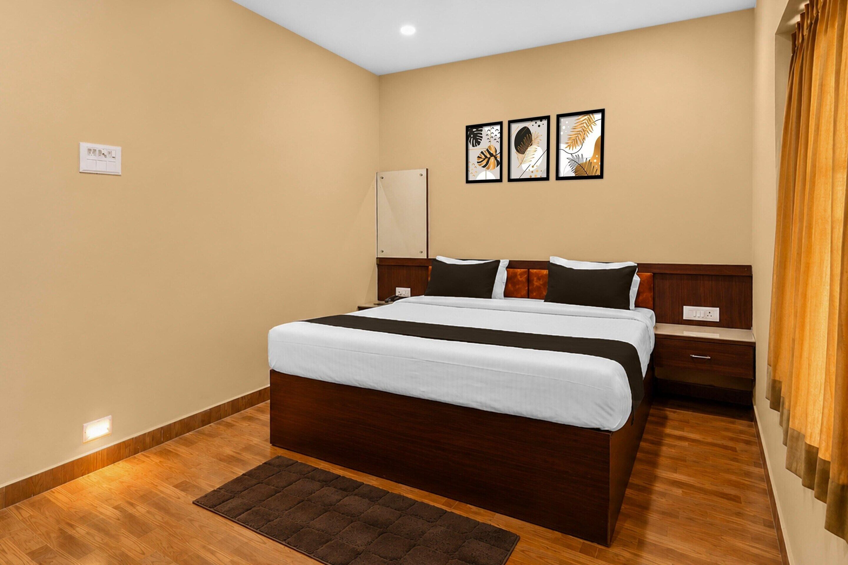 A hotel room with a large bed, a bedside table, a nightstand, a wall-mounted light, and a power outlet.