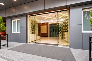 Entrada de un edificio moderno con puerta de vidrio, una planta en maceta y un banco de metal.