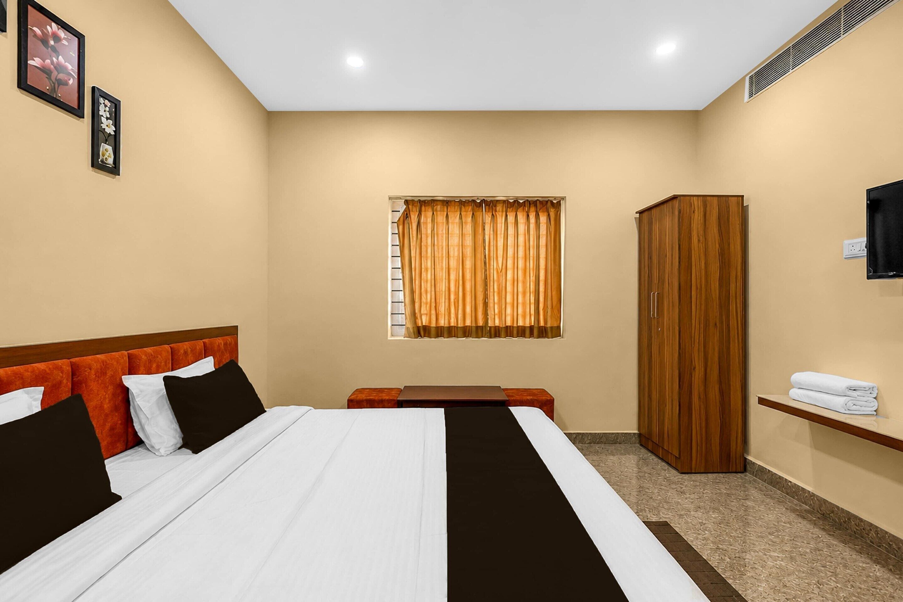 A hotel room with a bed, a wooden wardrobe, a small table, and a window with curtains.