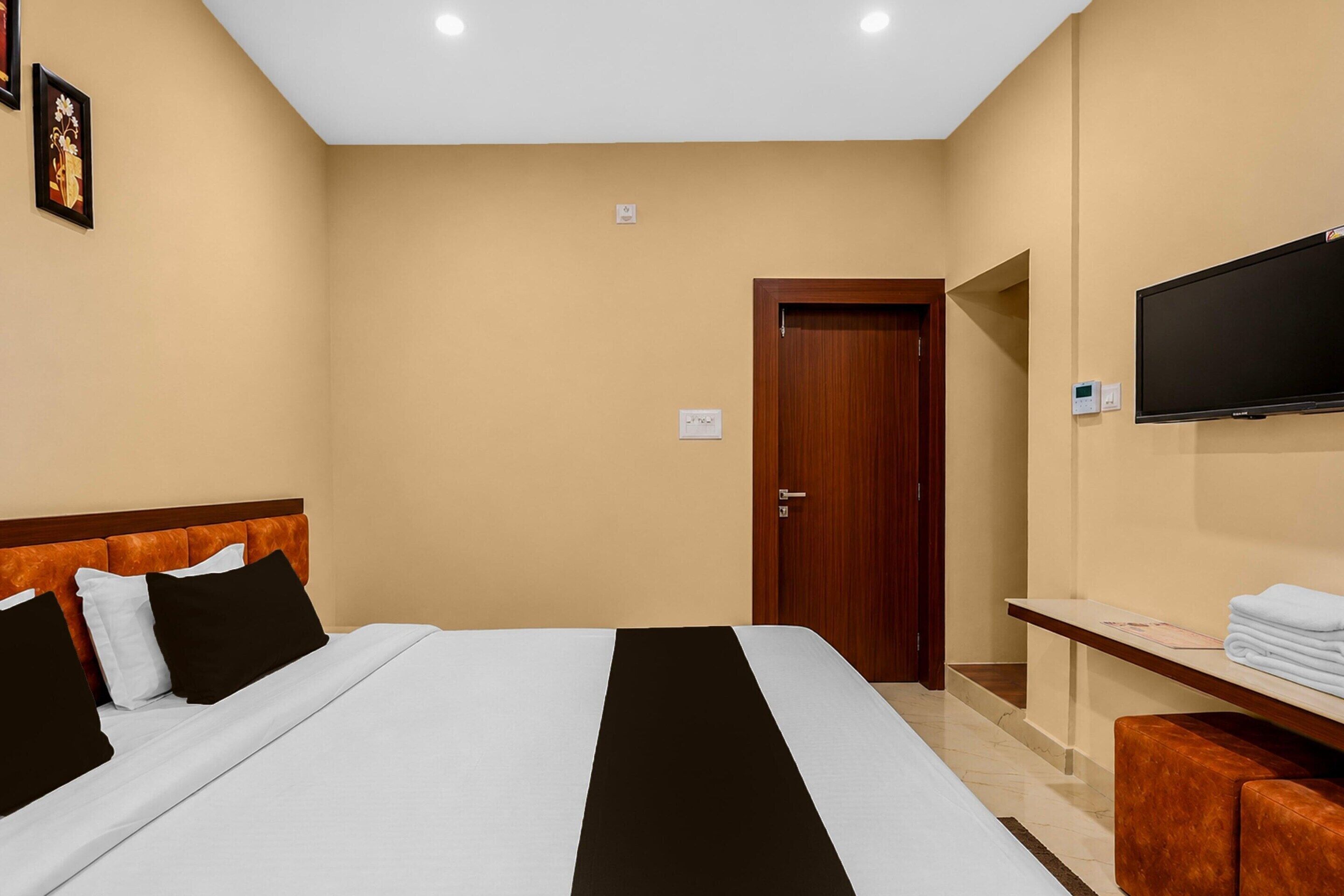 A hotel room with a bed, a television, a door, and a small table with towels.