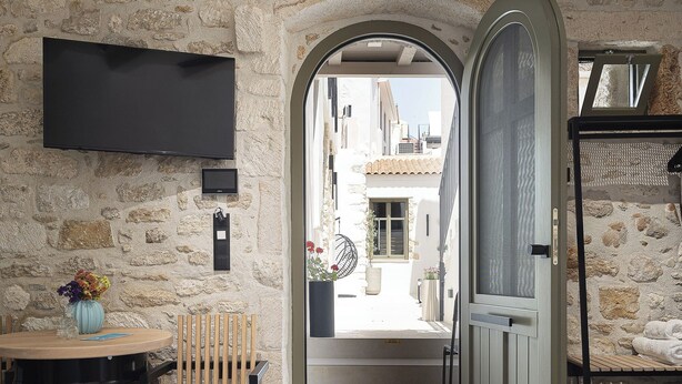 Una habitación con pared de piedra, una cama, un televisor montado en la pared, una silla y una pequeña mesa con un florero.