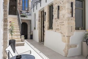 A courtyard with a stone wall, a staircase, a balcony with outdoor furniture, and a door leading to an interior space. - L10 Old Town Boutique Studios (Rethmyno)