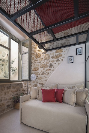 A room with a stone wall, a window, a sofa with cushions, and a ceiling fan. - L10 Old Town Boutique Studios (Rethmyno)