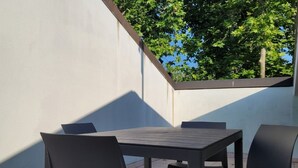 An outdoor patio with a table and chairs, a white wall, and a view of trees. - Location: in the central area, a few steps from the sea and all services.Description: very central four-room apartment on two floors connected by stairs.1st floor: large living room with sofa, table, kitchenette and dishwasher - bedroom with double bed - (Cesenatico)