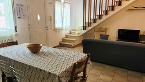 A dining area with a table and chairs, a staircase, a sofa, and a television. - Location: in the central area, a few steps from the sea and all services.Description: very central four-room apartment on two floors connected by stairs.1st floor: large living room with sofa, table, kitchenette and dishwasher - bedroom with double bed - (Cesenatico)