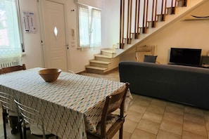 A dining area with a table and chairs, a staircase, a sofa, and a television. - Location: in the central area, a few steps from the sea and all services.Description: very central four-room apartment on two floors connected by stairs.1st floor: large living room with sofa, table, kitchenette and dishwasher - bedroom with double bed - (Cesenatico)