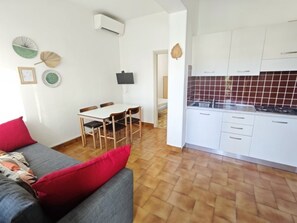 Ein kompakter Wohnbereich mit Essbereich, Küchenzeile und einem grauen Sofa mit roten Kissen.