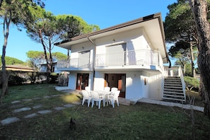 Ein zweistöckiges Haus mit Balkon, Treppe und Terrasse mit Gartenmöbeln.