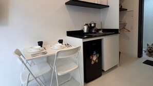 Et lille køkken med spisebord, stole, køleskab og en lille hund.
