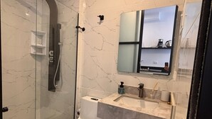 Et moderne badeværelse med en brusekabine med glasvægge, toilet, vask med et spejl over og en håndklædestang.