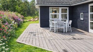 Ein Haus mit Terrasse, weißen Möbeln und einem blühenden Garten.
