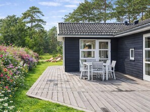 Ein Haus mit Terrasse, weißen Möbeln und einem blühenden Garten.