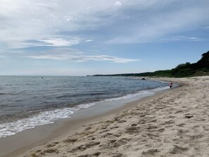A beach with a sandy shore, calm water, and a distant shoreline. - 5 Star Holiday Home in Aakirkeby (Akirkeby)