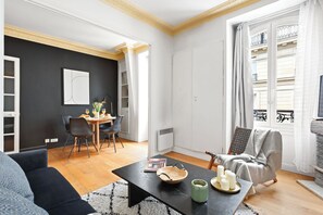 Ein modernes Wohnzimmer mit schwarzer Wand, einem Essbereich mit Tisch und Stühlen, einem Sofa, einem Couchtisch mit Kerzen und Blick auf einen Balkon.