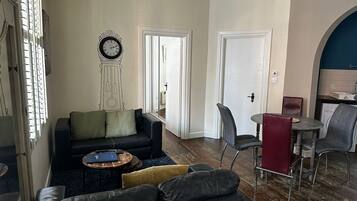 A living room with a sofa, a coffee table, a clock, and a dining area with chairs and a table.