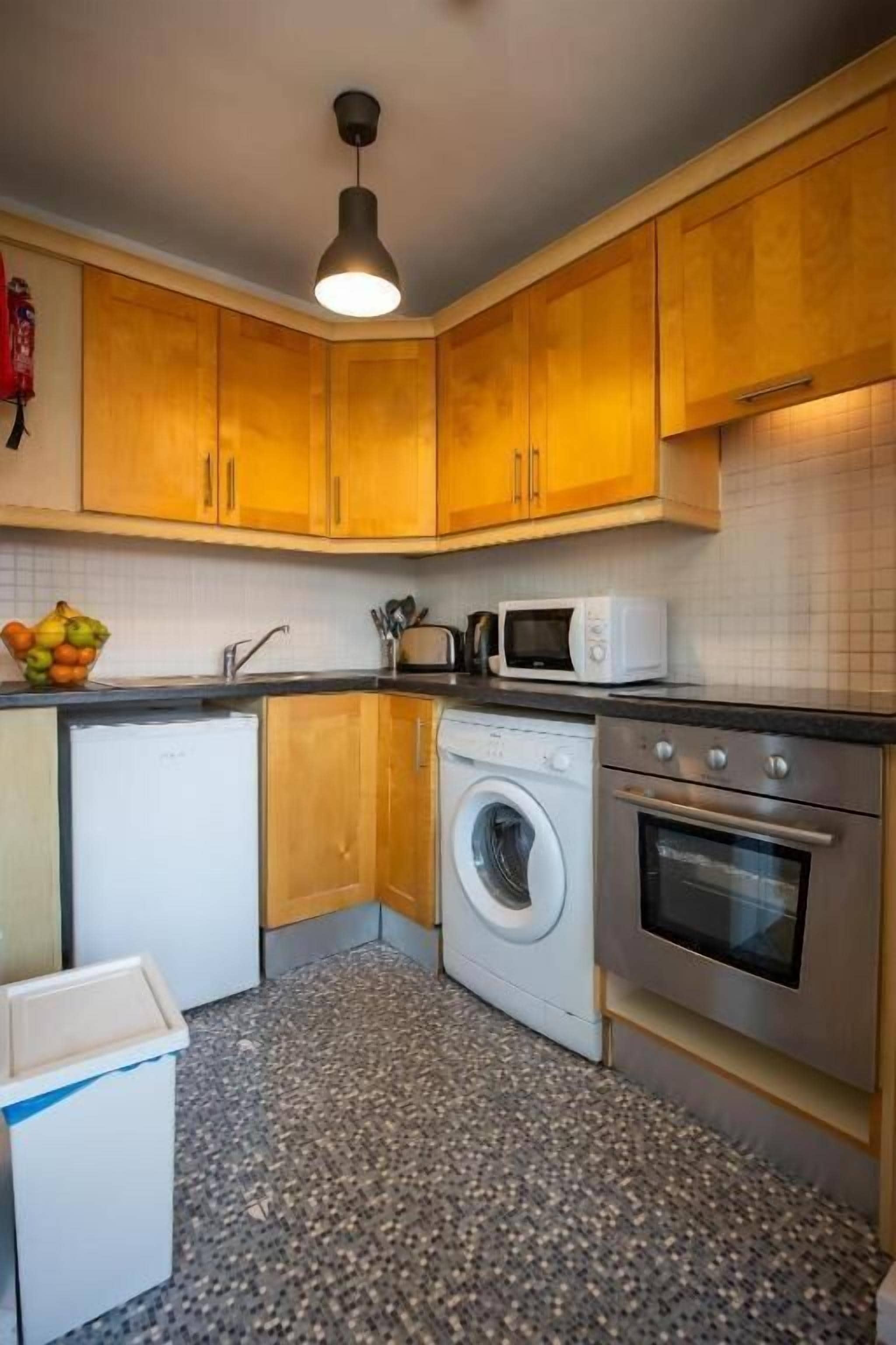 Cocina compacta con armarios de madera, lavadora, microondas y horno empotrado.
