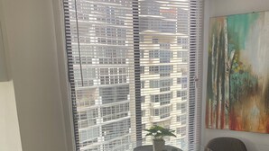 A room with a glass table and two chairs, a window with blinds, a potted plant, and a painting on the wall. - 3-ROOM APARTMENT IN PUNTA PAITILLA WITH OPEN-PLAN KITCHEN, PARKING, WIFI, AND VISTASKY BUILDING (Panamá)