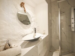 Un bany amb un lavabo rodó, un mirall, una tovallola i una zona de dutxa.