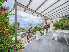 Une terrasse extérieure couverte, dotée d’une table et de chaises, entourée de verdure et offrant une vue sur le paysage urbain.
