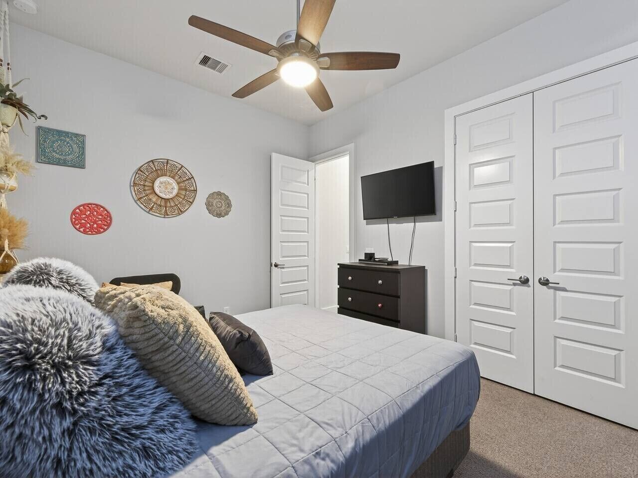 Une chambre à coucher avec un lit, une commode, un téléviseur et un ventilateur de plafond.