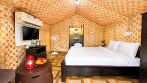 A hotel room with a bed, a TV, a fan, a red lantern, and a small table with a basket of fruit. - Sumitel Araku Mount View Camping Resort (Araku Valley)