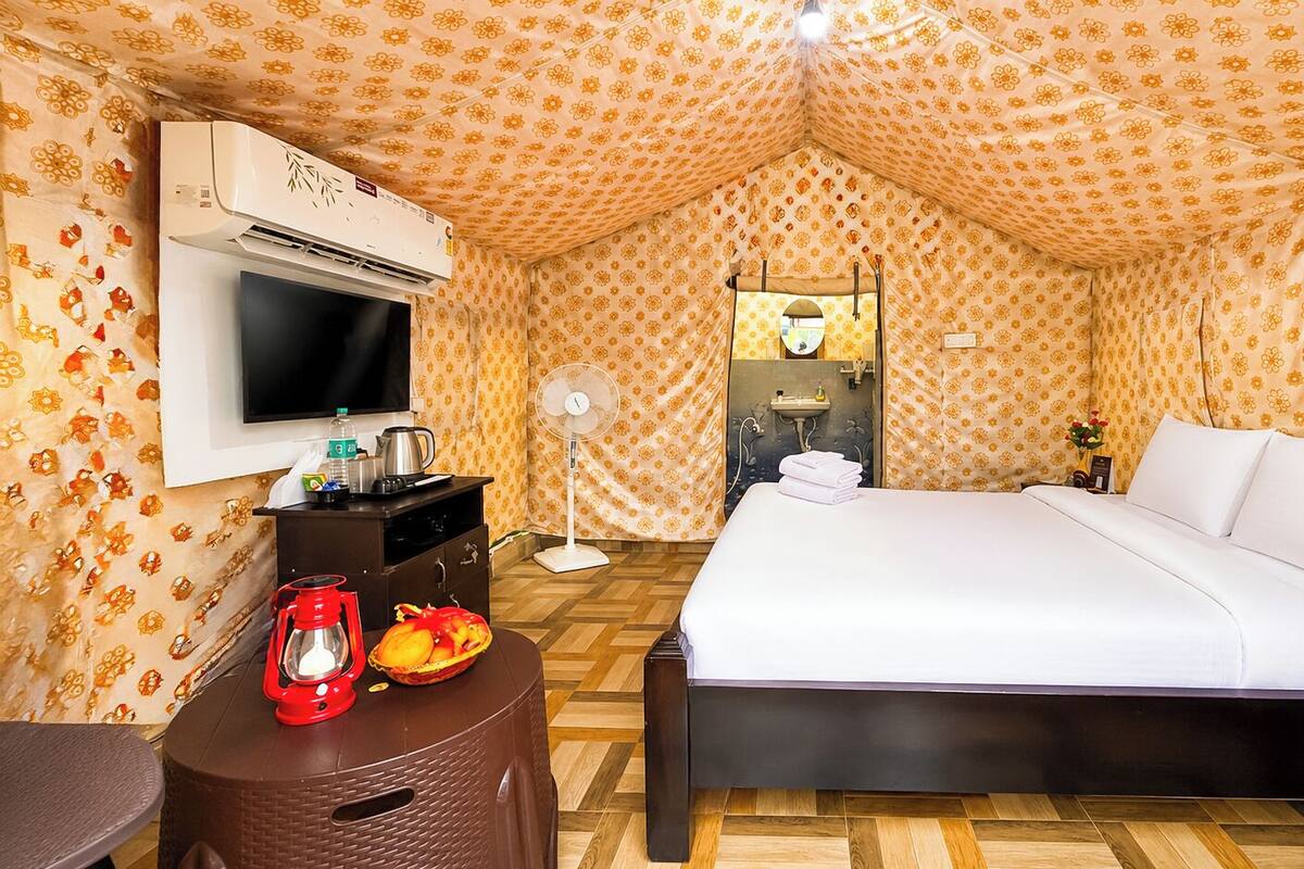 Una habitación de hotel con una cama, un televisor, un ventilador, un farol rojo y una mesa pequeña con una cesta de fruta.