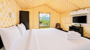 Habitación de hotel con cama, escritorio, silla, televisión y ventana con vistas a zonas verdes y montañas.