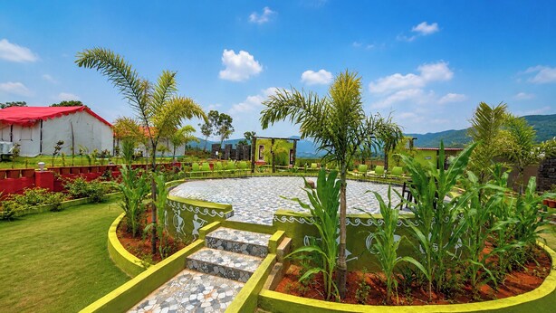 A landscaped outdoor area with a circular stone pathway, green seating, and a building with a red roof. - Sumitel Araku Mount View Camping Resort (Araku Valley)