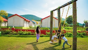 A playground with swings and a grassy area, surrounded by buildings with red roofs and greenery. - Sumitel Araku Mount View Camping Resort (Araku Valley)