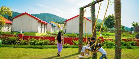 A playground with swings and a grassy area, surrounded by buildings with red roofs and greenery.