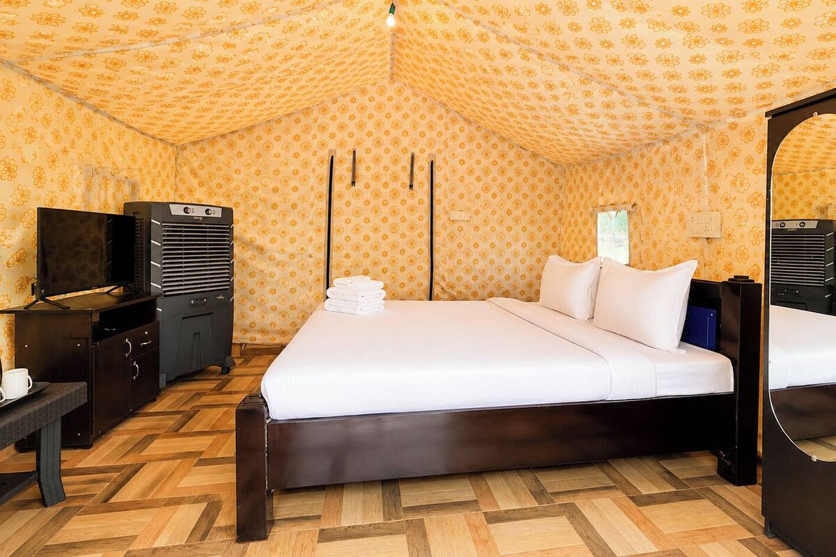 Una habitación con cama, escritorio con tetera, televisión y armario.