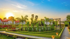 A garden with a pathway, palm trees, and a building with a green facade. - Sumitel Araku Mount View Camping Resort (Araku Valley)