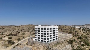 A modern white building with a rectangular shape, surrounded by a stone wall, set in a dry, hilly landscape.