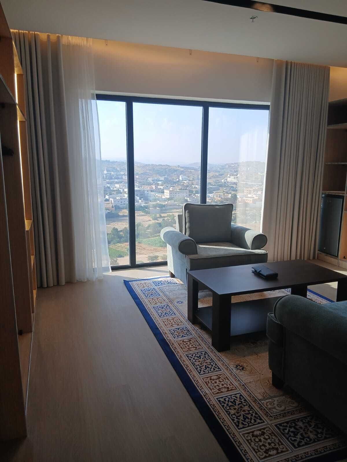 A modern living room with a large window, a sofa, a coffee table, and a patterned rug.